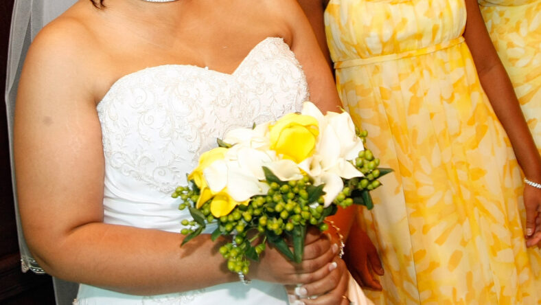 Stock image of a bride holding her bouquet next to her bridesmaid in yellow