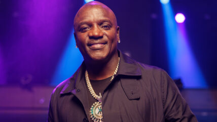 Akon wearing a black top with a large gold necklace on a music video taping