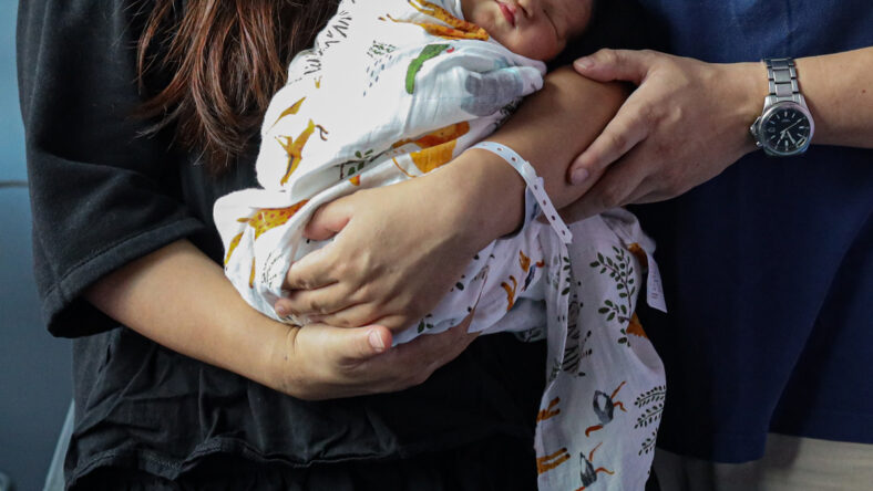 Stock image of a woman holding a swaddled newborn in her arms