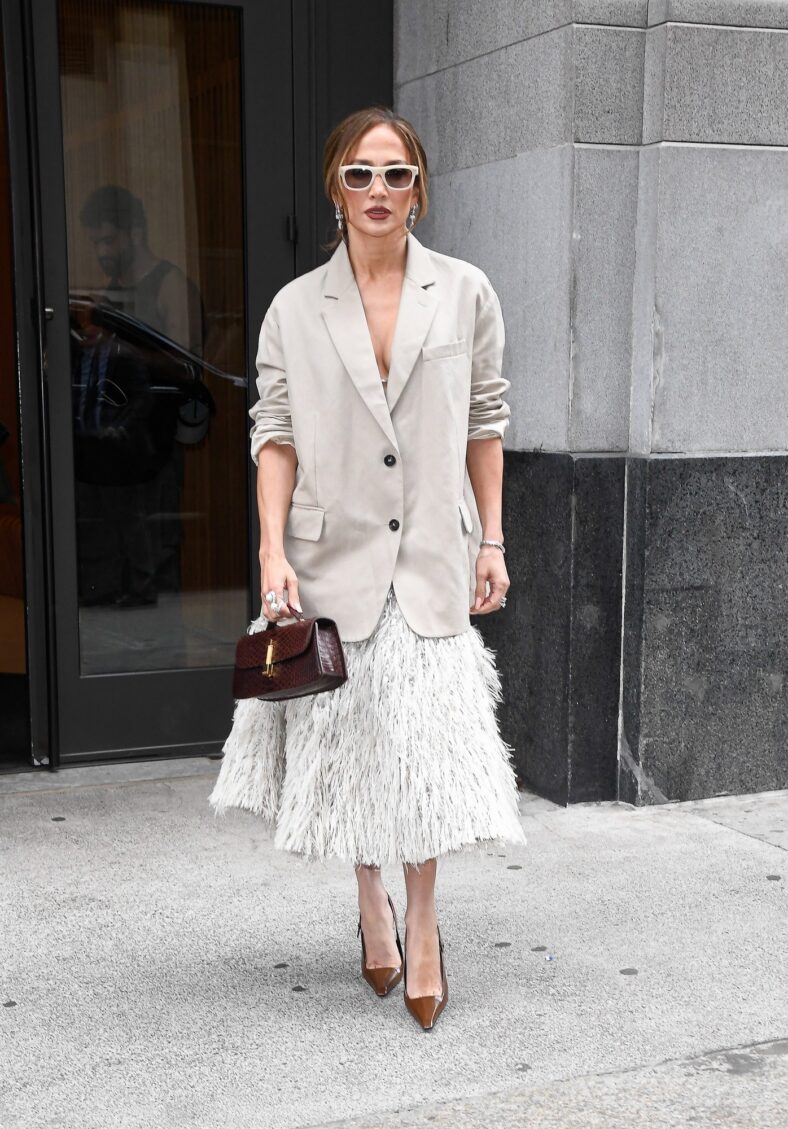 Jennifer Lopez steps out in a loose, oversized beige blazer. She has her hair up and is wearing sunglasses and carrying a leather handbag.