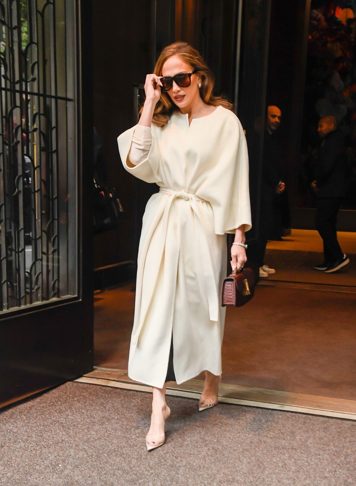 Jennifer Lopez wears a cream-colored wrap coat with wide sleeves and oversized sunglasses.