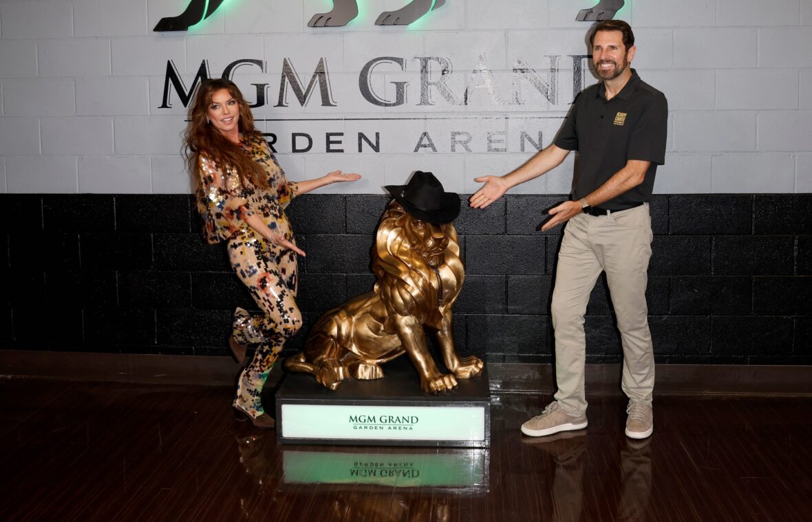 Shania Twain em um macacão de lantejoulas multicoloridas posa com o CEO da ACM, Damon Whiteside, com a estátua de Leo, o Leão.