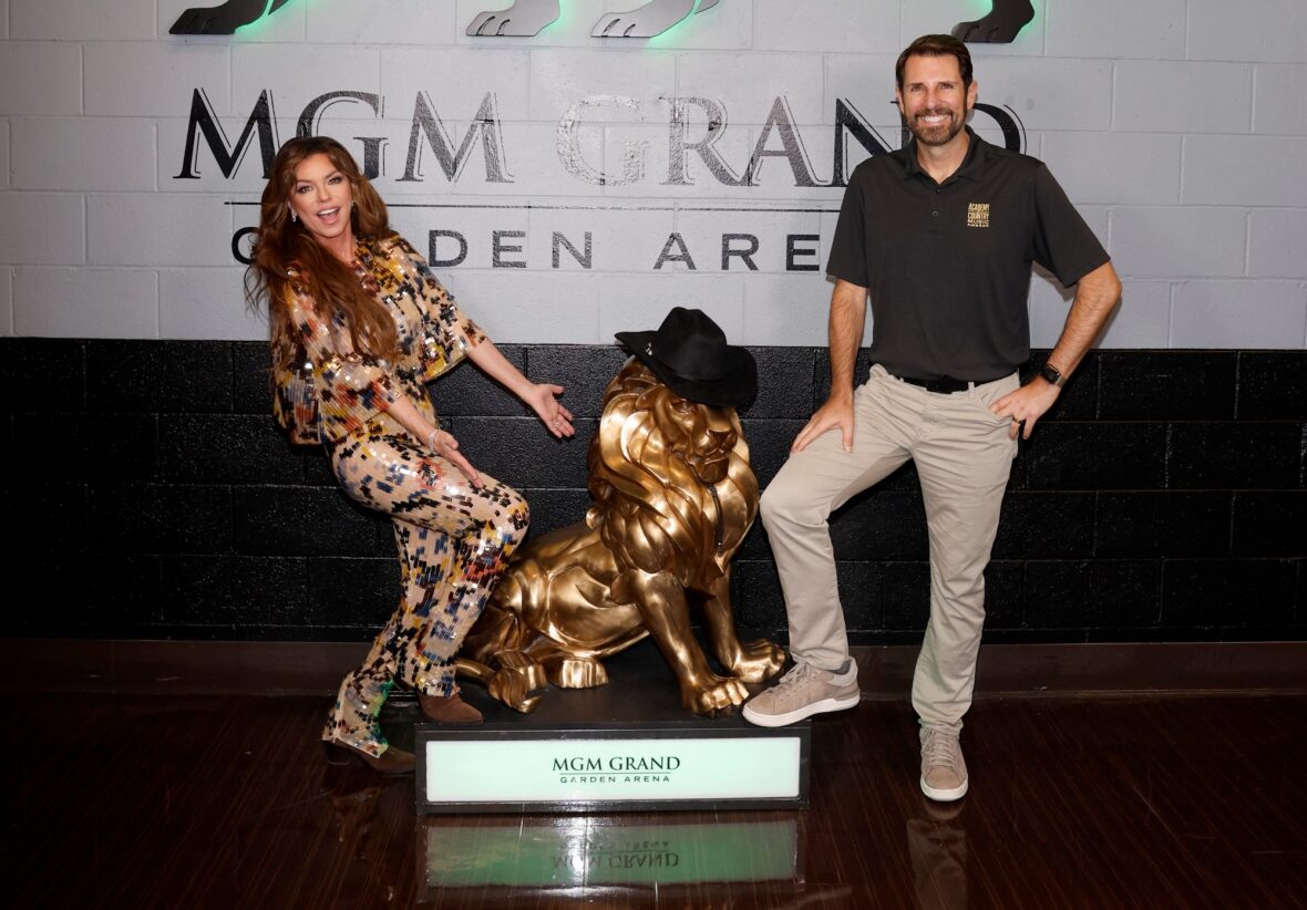 Shania Twain em um macacão de lantejoulas multicoloridas posa com o CEO da ACM, Damon Whiteside, com a estátua de Leo, o Leão.