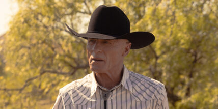 Ed Harris in character for Dutton Ranch, wearing a cowboy hat in a field