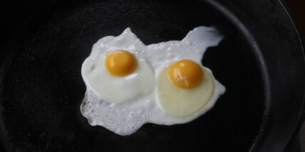 two sunny side up eggs cooking in a cast iron skillet