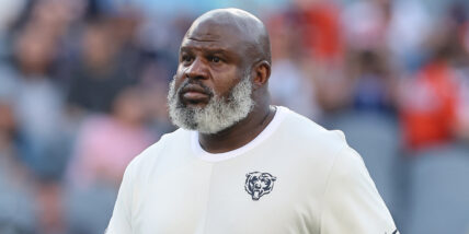 Eric Bieniemy on an NFL field walking with a blurry crowd behind him