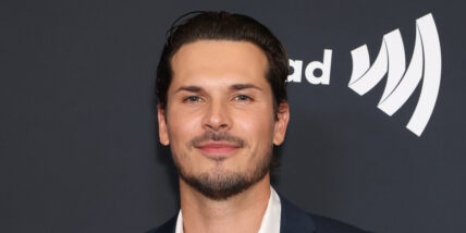 Gleb Savchenko posing in front of a black background with an obscured white logo