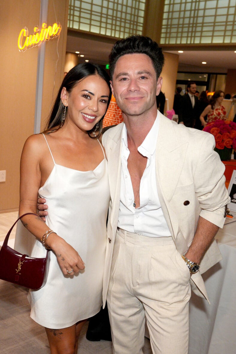 Janel Parrish and Sasha Farber at an event coordinating in white outfits. They are posing together and smiling for the camera