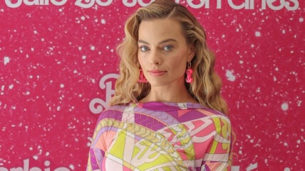 Margot Robbie poses in front of a glittery pink Barbie background.