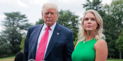 Karoline Leavitt and Donald Trump standing outside together in Washington DC. He's in a suit with a red tie and she's wearing green