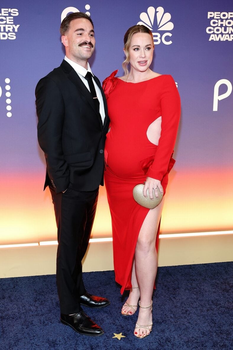 Conner Leavitt and a pregnant Whitney Leavitt pose together at an event. Conner in a black suit and Whitney in a red cutout dress.