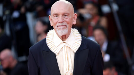 John Malkovich attends the Venice Film Festival in a black shirt with a white collar.