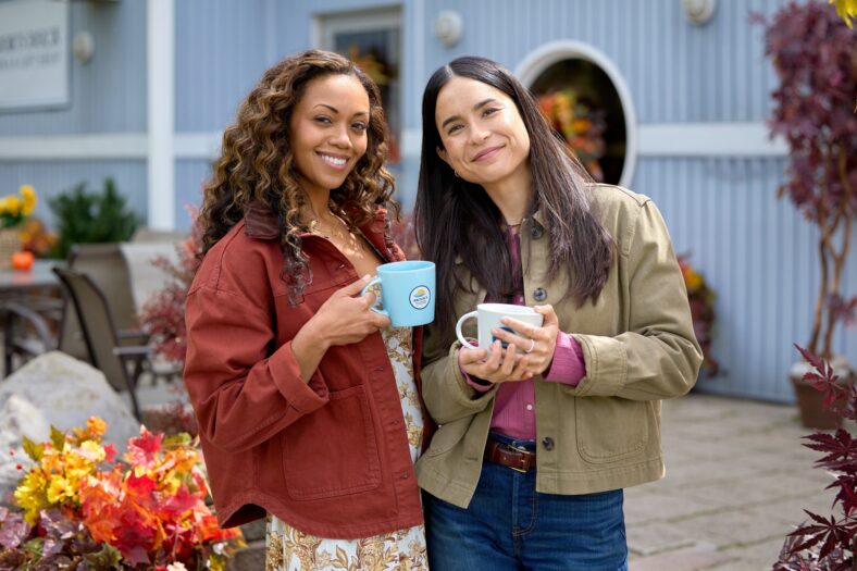 Mishael Morgan and Jenny Raven holding coffee mugs in a photo from Pumpkin Regatta Romance.