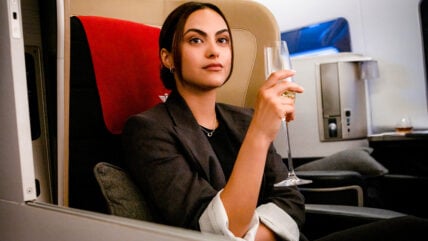 Camila Mendes holding a glass of champagne in first class in a still from Upgraded.