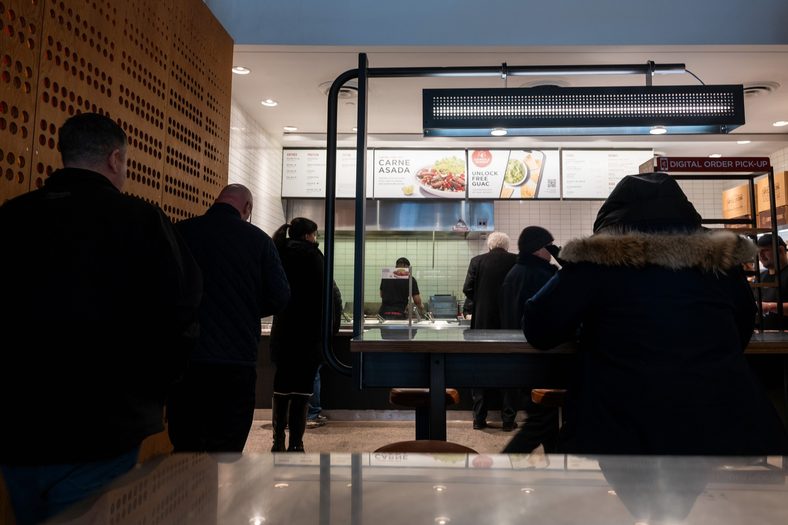 Photo of customers waiting in line inside of a Chipotle store