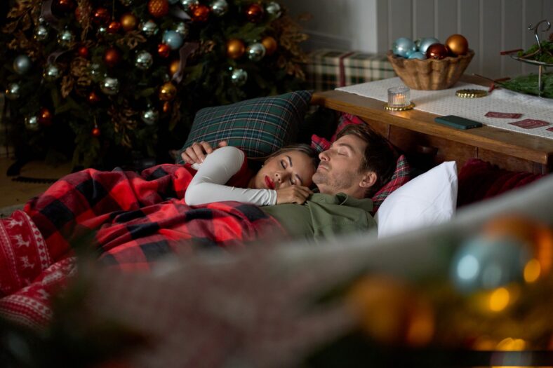 Janel Parrish and Daniel Lissing cuddle together on a couch in still from Forgotten Holiday.