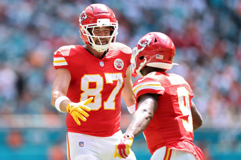 Kenneth Walker in a Chiefs game, with his back to the camera, going to high five Travis Kelce who is facing the camera