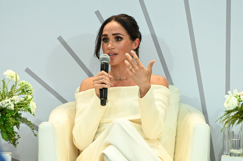 Meghan Markle speaking into a microphone in a white outfit on stage