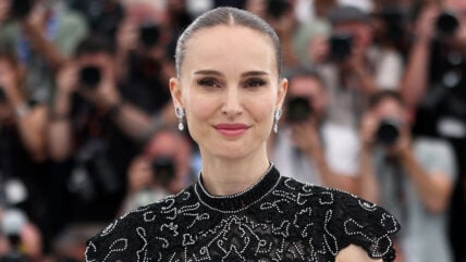 Natalie Portman smiling at Cannes Film Festival in front of many photographers blurred out in the background