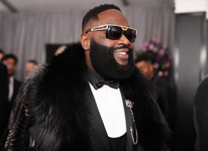 Rick Ross smiling looking to the side on a red carpet in a stock image